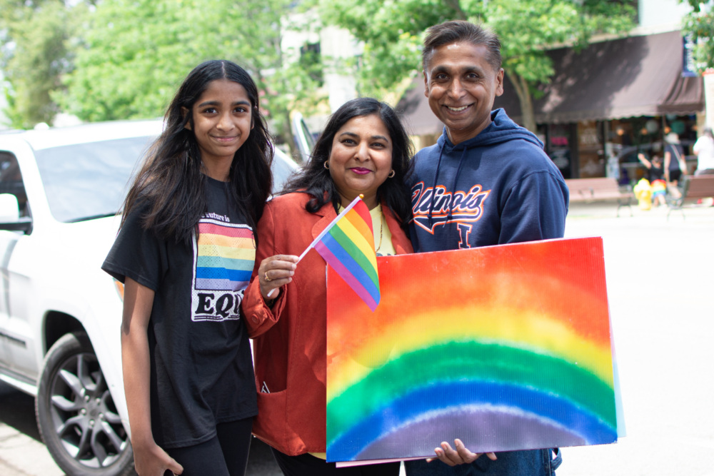 a family holding a pride flag and rainbow painting.